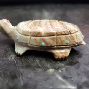 Pode incluir: Uma figura de tartaruga esculpida em pedra marrom e branca com detalhes turquesa.