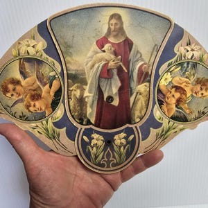 Abanico de papel tríptico, Jesucristo sosteniendo un corderito rodeado de una gran oveja, ángeles querubines a cada lado, publicidad en la parte posterior.