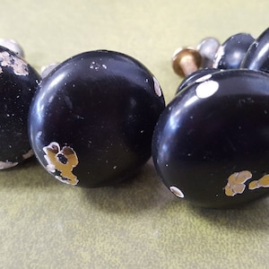 May include: Six black cabinet knobs with gold and white accents. The knobs are round and have a slightly distressed finish.