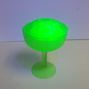May include: A green glass vase with a wide, round bowl and a tall, slender stem. The vase has a frosted finish and a unique, textured design.