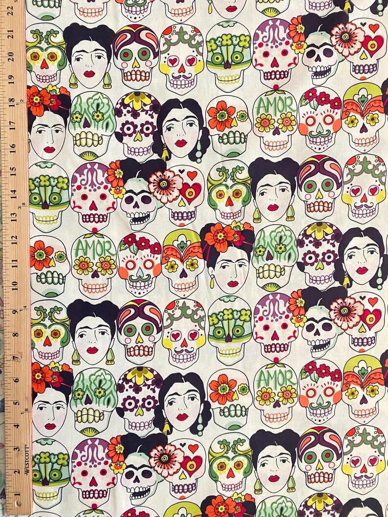 Puede incluir: Una tela blanca con un patr&oacute;n repetido de calaveras de az&uacute;car coloridas y dise&ntilde;os florales. Las calaveras tienen ojos negros, labios rojos y est&aacute;n decoradas con flores y la palabra "AMOR".