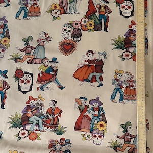 Puede incluir: Una tela blanca con un patrón repetido de esqueletos vestidos con ropa tradicional mexicana. Los esqueletos están bailando, tocando música y sosteniendo flores. También hay calaveras de azúcar y diseños florales en toda la tela.
