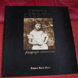 May include: A black hardcover book with gold lettering on the front cover. The title is "Lewis Carroll, fotografo vittoriano" and the author is "Franco Maria Ricci". The cover features a black and white photograph of a young girl.