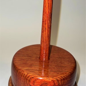 Puede incluir: Un cuenco de lana de madera con un huso alto y puntiagudo. El cuenco y el huso están teñidos de un rico color marrón rojizo y tienen un acabado brillante.