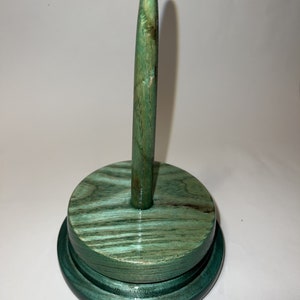 May include: A green wooden yarn bowl with a tall, pointed spindle. The bowl has a dark green base and a lighter green top.