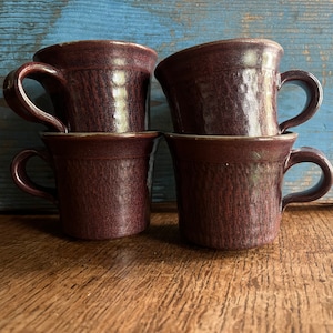 Puede incluir: Cuatro tazas de cerámica marrón apiladas una encima de la otra. Las tazas tienen un acabado texturizado y moteado.