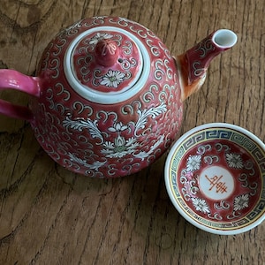 May include: A red and white porcelain teapot with a floral design and a matching teacup. The teacup has a red and white floral design with a Chinese character in the center.