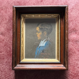 Puede incluir: Retrato enmarcado de un niño pequeño con una chaqueta azul, sobre un fondo oscuro y con un marco dorado. La firma del artista es visible en la esquina inferior derecha.