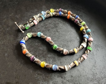 May include: A silver necklace with a toggle clasp features colorful glass beads with a striped pattern. The beads are interspersed with silver spacers.