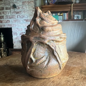 Könnte beinhalten: Eine Keramikskulptur mit einer strukturierten, organischen und abstrakten Form. Die Skulptur ist braun und beige mit einer rauen, unebenen Oberfläche.