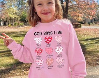 May include: Pink sweatshirt with the text "GOD SAYS I AM" and a series of hearts with bible verses and words like "Strong", "Enough", "Brave", "Unique", "Victorious", "Chosen", "Always Loved", "Capable", and "Beautiful".