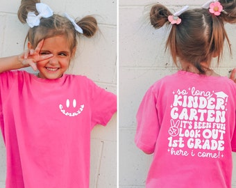 May include: Pink t-shirt with a white smiley face on the front and the text "so long KINDERGARTEN it's been fun LOOK OUT 1st GRADE here i come!" on the back.