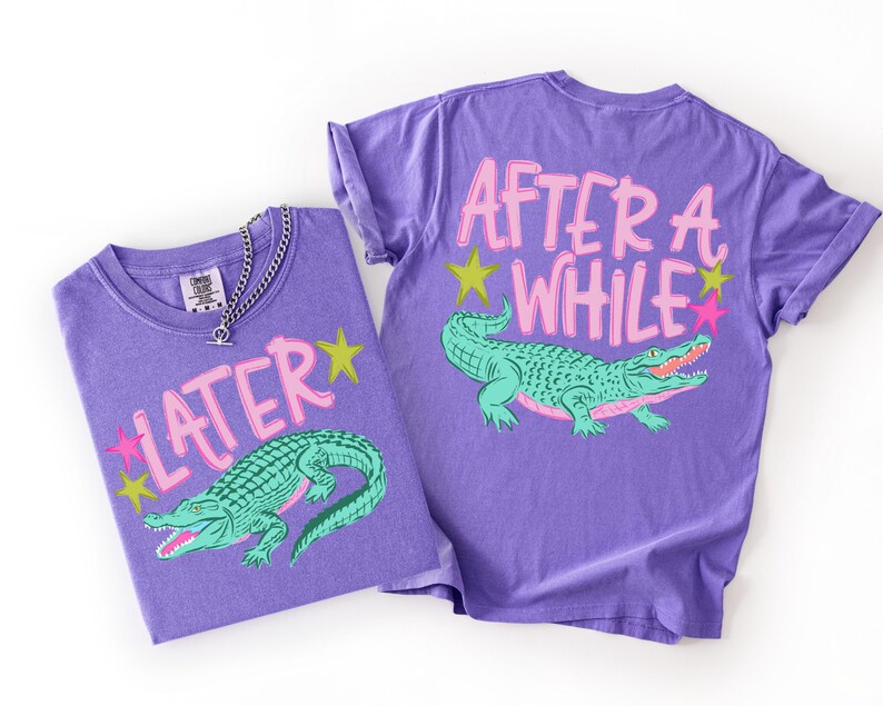 May include: Two purple t-shirts with matching designs. One shirt displays the word "LATER" with a green alligator graphic and star accents. The other shirt has the words "AFTER A WHILE" and a similar alligator design.