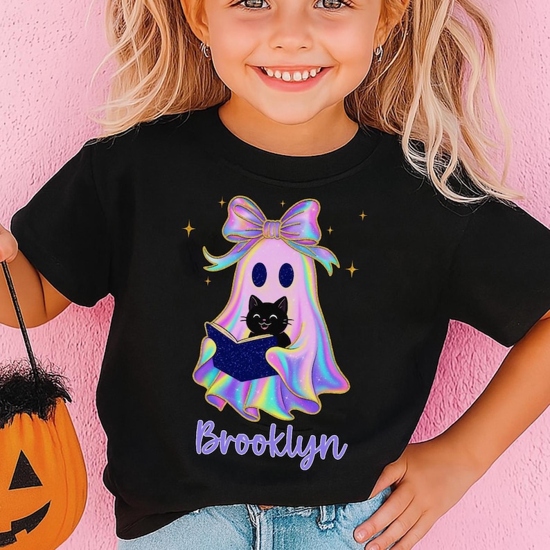 little girl wearing black halloween shirt with a cute preppy ghost with coquette bow and a trendy iridescent look , personalized with her name