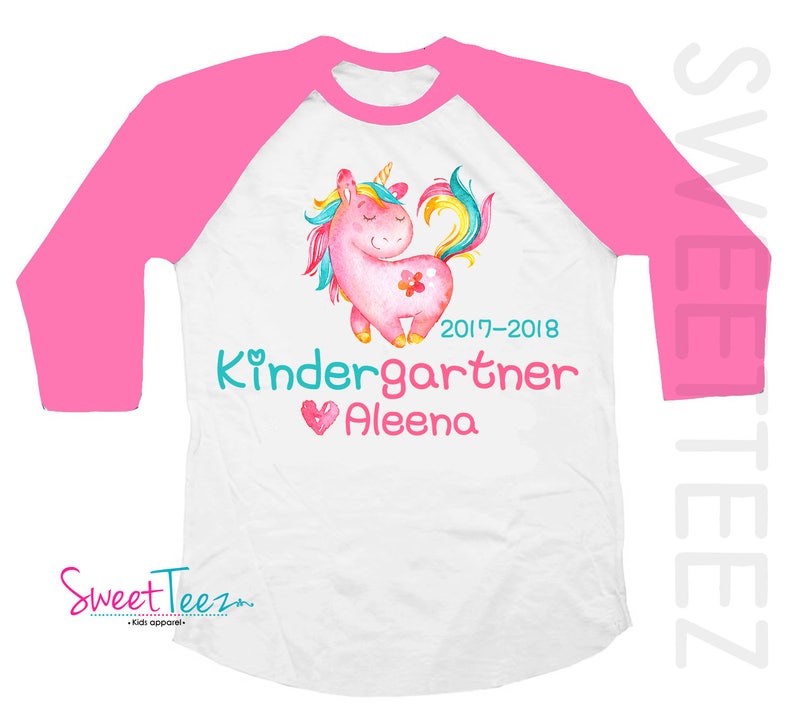 Pode incluir: Camiseta branca e rosa estilo raglan com um design de unic&oacute;rnio em aquarela. O unic&oacute;rnio &eacute; rosa com uma crina e cauda coloridas. A camiseta tem o texto "Kindergartner Aleena" e o ano "2017-2018".