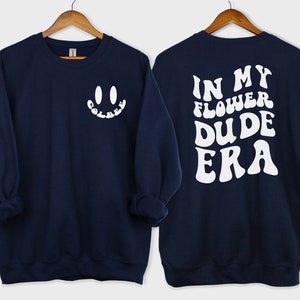 May include: Navy blue sweatshirt with a white smiley face on the front and the text "IN MY FLOWER DUDE ERA" in white on the back.