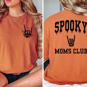 Pu&ograve; includere: Maglietta arancione con una grafica di mano scheletrica nera sul davanti e il testo "SPOOKY MOMS CLUB" con un effetto gocciolante e una grafica di mano scheletrica sul retro.