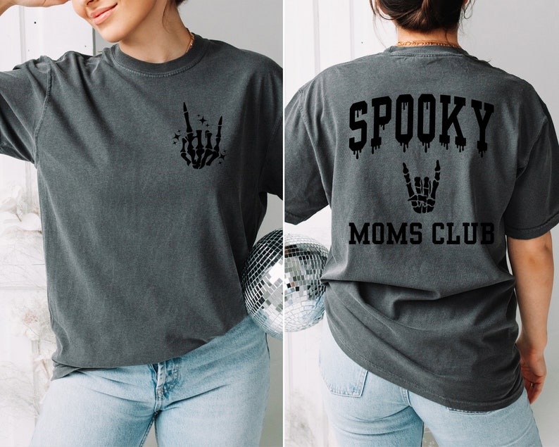 Pu&ograve; includere: Una maglietta grigio scuro con una mano scheletrica che fa un segno rock and roll sul davanti e il testo "SPOOKY MOMS CLUB" con un effetto gocciolante e una mano scheletrica che fa un segno rock and roll sul retro.