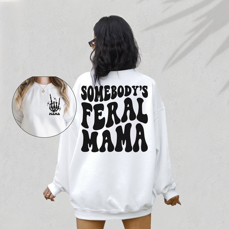 May include: White sweatshirt with the text "SOMEBODY'S FERAL MAMA" in black, retro-style lettering on the back. A smaller image on the front shows a skeleton hand making a rock-and-roll gesture, with the word "Mama" below.