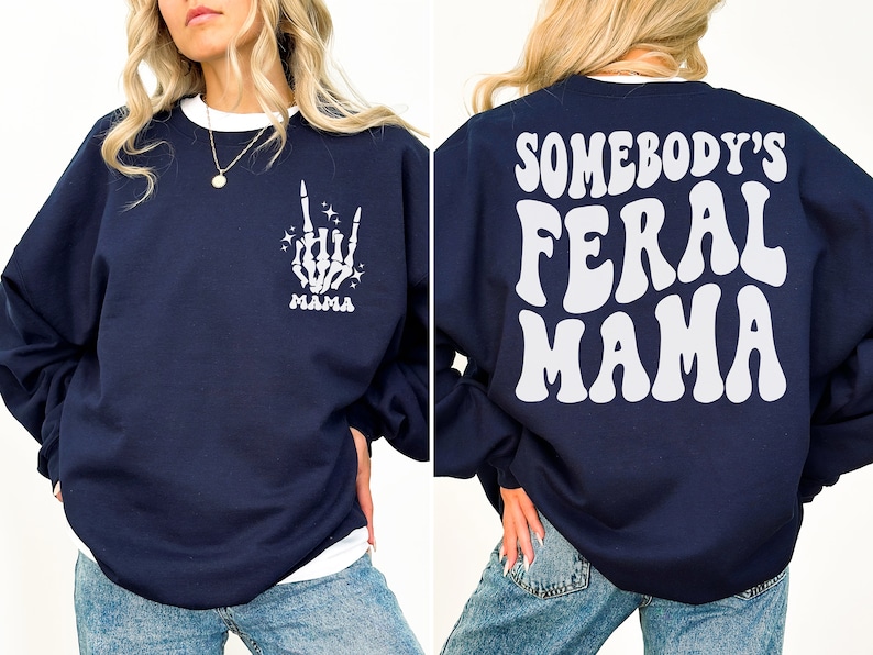 May include: Navy blue sweatshirt with white text and graphics. The front features a skeleton hand with the word "MAMA" below it. The back of the sweatshirt says "SOMEBODY'S FERAL MAMA" in large, white, retro-style lettering. The sweatshirt has a white crew neck.