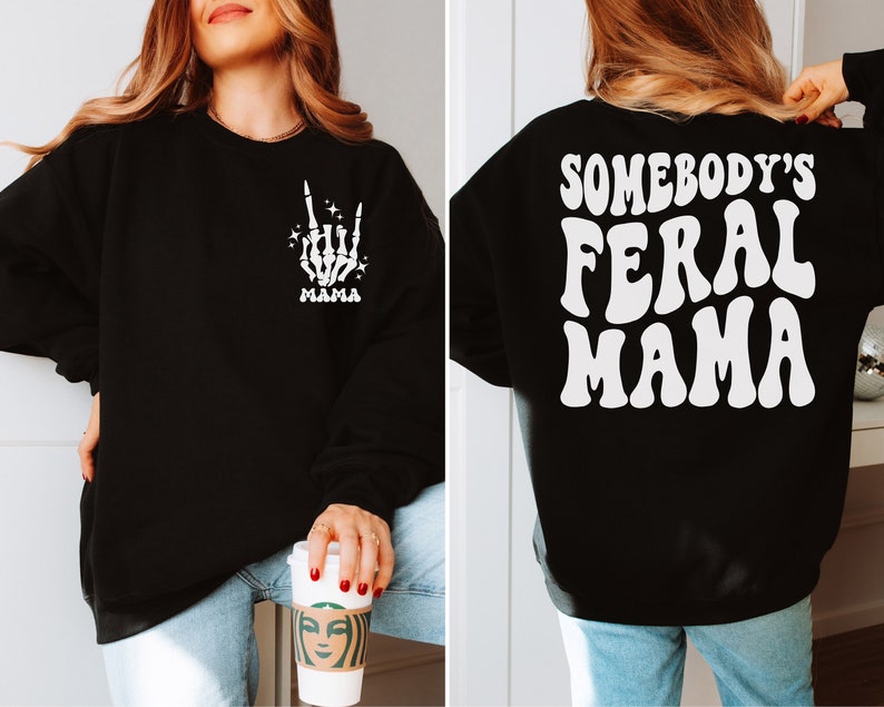 May include: Black sweatshirt with white text and graphics. The front features a skeleton hand with the word "MAMA". The back of the sweatshirt says "SOMEBODY'S FERAL MAMA" in a retro font.