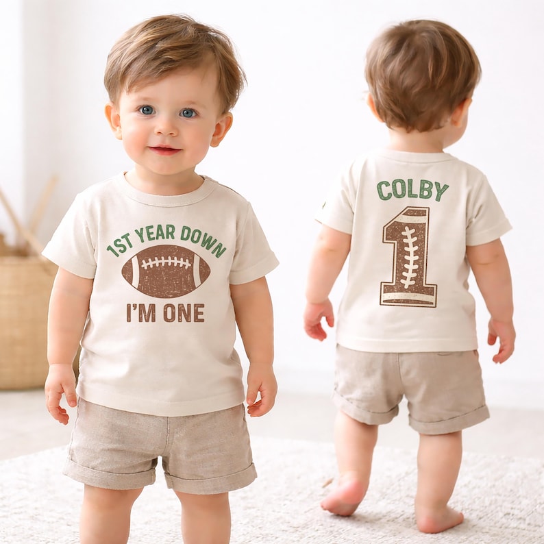 baby boy wearing first birthday shirt front and back with football that says 1st year down im one on the front and a big 1 with football pattern on the back personalized with his name