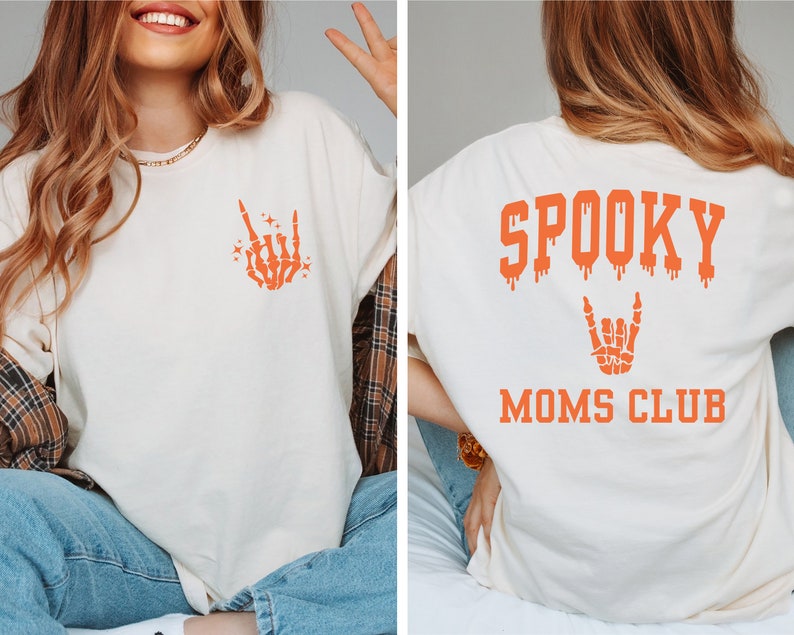 Pu&ograve; includere: Una maglietta bianca con un disegno di mano scheletrica arancione sul davanti e il testo "SPOOKY MOMS CLUB" sul retro.