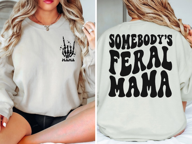 May include: Cream-colored sweatshirt with a black skeleton hand graphic making a rock-on gesture and the word "MAMA" below it. The back of the sweatshirt features the text "SOMEBODY'S FERAL MAMA" in a retro font.