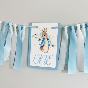 Peter Rabbit high chair banner featuring either a blue Peter Rabbit, pink Peter Rabbit, yellow Peter Rabbit or Green Peter Rabbit. The fabric will coordinate with the color of Peter Rabbit's jacket. The banner is available to read an age or name.