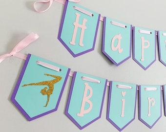 Könnte beinhalten: Ein türkisfarbenes und violettes Banner mit den Worten "Happy Birthday" in rosa Buchstaben. Das Banner zeigt eine goldene Glitzer-Gymnastik-Silhouette.