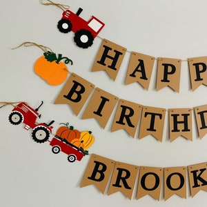 May include: A brown banner with the words "Happy Birthday Brooks" in black letters. The banner is decorated with red tractors, pumpkins, and fall leaves.