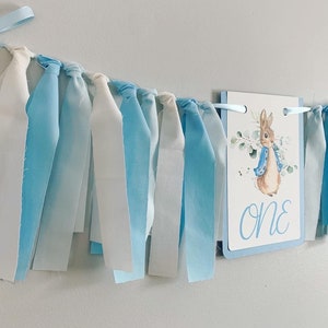 Peter Rabbit high chair banner featuring either a blue Peter Rabbit, pink Peter Rabbit, yellow Peter Rabbit or Green Peter Rabbit. The fabric will coordinate with the color of Peter Rabbit's jacket. The banner is available to read an age or name.