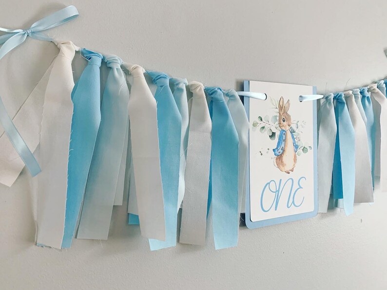 Peter Rabbit high chair banner featuring either a blue Peter Rabbit, pink Peter Rabbit, yellow Peter Rabbit or Green Peter Rabbit. The fabric will coordinate with the color of Peter Rabbit's jacket. The banner is available to read an age or name.