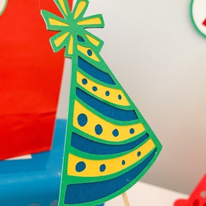 primary colors birthday centerpiece table decor that includes a party hat, number and birthday gifts made of layered cardstock