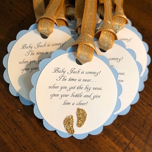 May include: Blue and white favor tags with gold glitter accents. The tags feature the text "Baby Jack is coming! The time is near... when you get the big news, open your bottle and give him a cheer!"