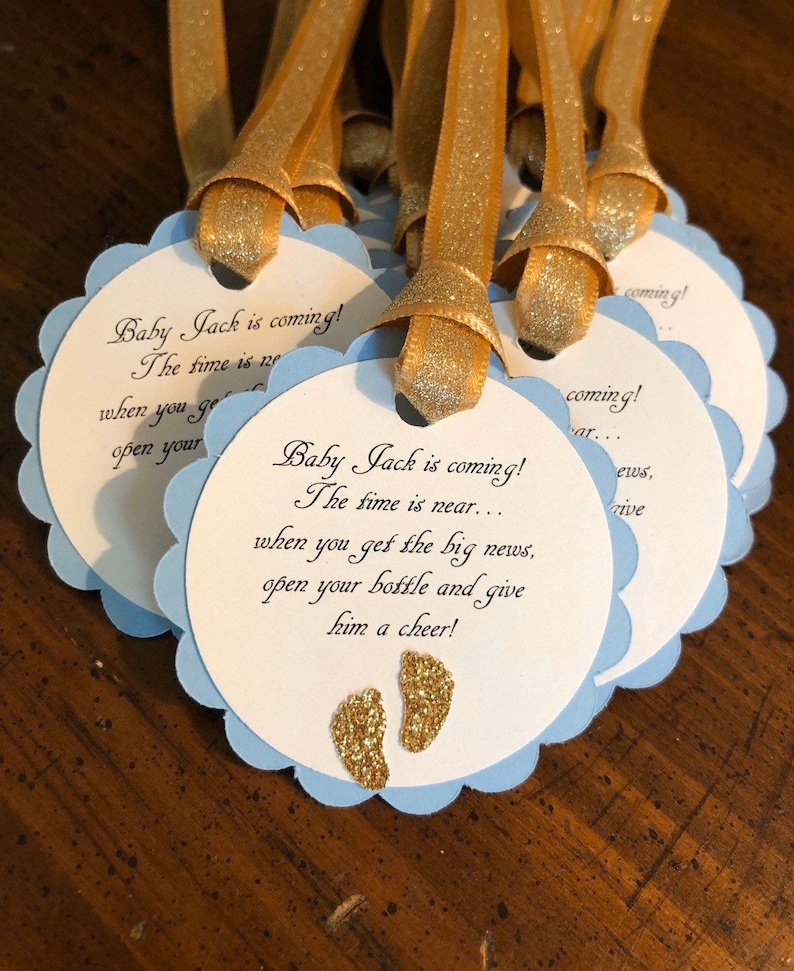 May include: Blue and white favor tags with gold glitter accents. The tags feature the text "Baby Jack is coming! The time is near... when you get the big news, open your bottle and give him a cheer!"