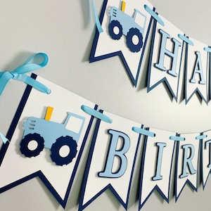 May include: A blue and white banner with the words "Happy Birthday" and a blue tractor illustration. The banner is strung together with blue ribbon.