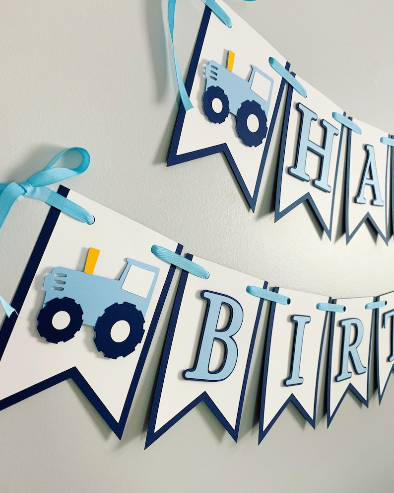 May include: A blue and white banner with the words "Happy Birthday" and a blue tractor illustration. The banner is strung together with blue ribbon.