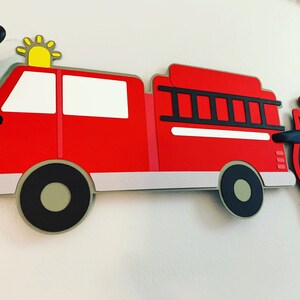 May include: Red fire engine paper cutout with a black ladder, white windows, and black wheels. The engine has a yellow star on top. The cutout is part of a fire engine themed banner.