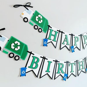 May include: Green and white paper banner with the words "Happy Birthday" in green letters with black outlines. The banner is decorated with small blue recycling bins and green garbage trucks with recycling symbols.