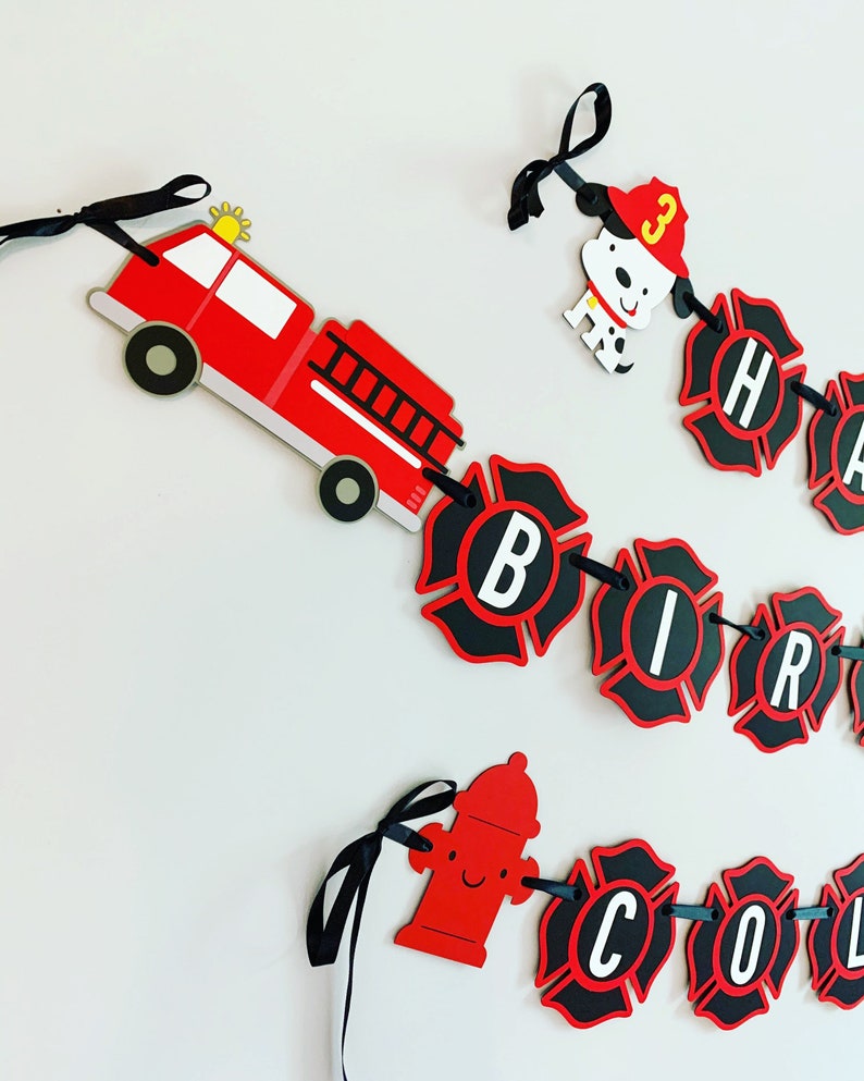 May include: Red and black firefighter themed birthday banner with the words "Happy Birthday" and a fire engine, fire hydrant, and dalmatian dog.