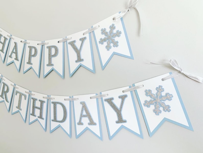 May include: A blue and white banner with silver glitter letters that reads "Happy Birthday". The banner has two silver glitter snowflakes.
