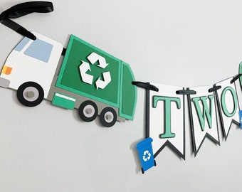 May include: Green and white recycling truck with a recycle symbol on the side, a black and white banner with the word "TWO" in green letters, and a blue recycling bin with a recycle symbol on it.