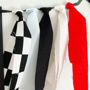 Op de afbeelding: Een banner met zes stofstroken in zwart-wit geruit, lichtblauw, zwart, wit, rood en zwart. De stroken zijn aan elkaar gebonden met een zwart lint.