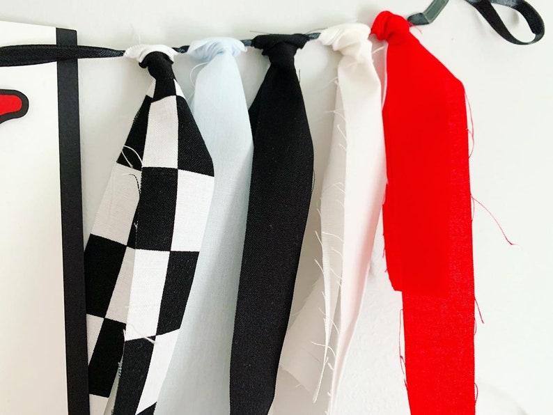 Op de afbeelding: Een banner met zes stofstroken in zwart-wit geruit, lichtblauw, zwart, wit, rood en zwart. De stroken zijn aan elkaar gebonden met een zwart lint.