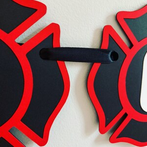 May include: Two red and black firefighter helmet cutouts connected by a black ribbon.