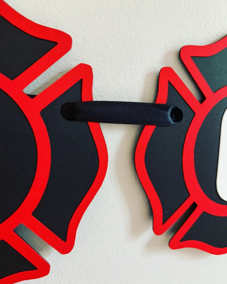 May include: Two red and black firefighter helmet cutouts connected by a black ribbon.