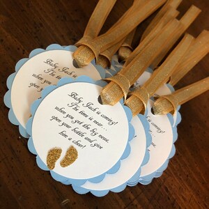 May include: Blue and white scalloped circle favor tags with gold glitter accents. The tags have the text "Baby Jack is coming! The time is near... when you get the big news, open your bottle and give him a cheer!"