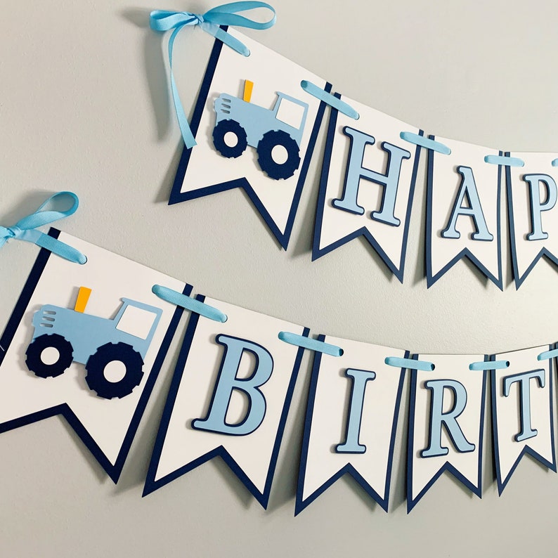 May include: A blue and white banner with the words "Happy Birthday" and two blue tractors. The banner is strung with blue ribbon.