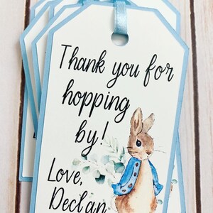 Peter Rabbit "Thank you for hopping by" birthday or baby shower party favor tags. The color of Peter Rabbit's jacket is customizable and can be changed from blue to pink, green or yellow. The background and ribbon will coordinate with Peter Rabbit's Jacket. The text is also customizable.